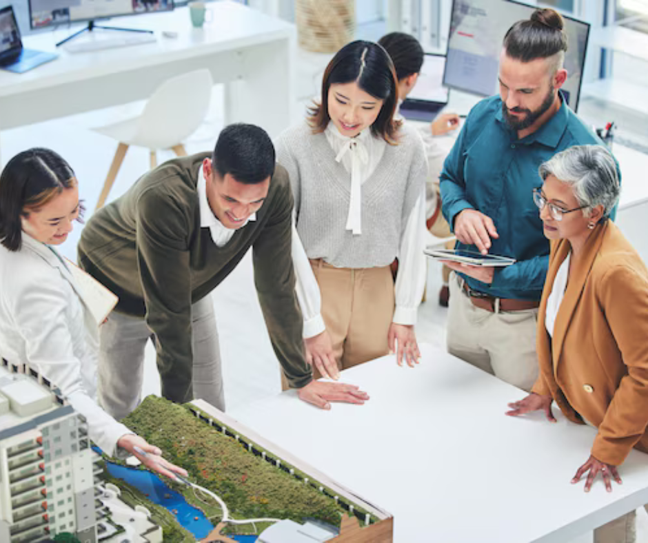 A group of diverse professionals collaborate around a model, discussing a project in a bright office.