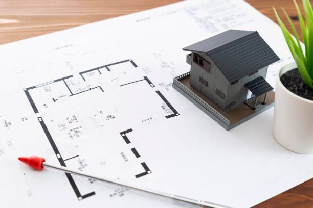 Floor plan with a miniature house and plant. A pen points to the plans.