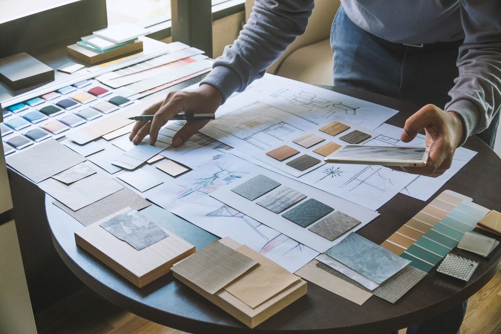 Person working on interior design concepts, with sketches, color swatches, and material samples on a table.