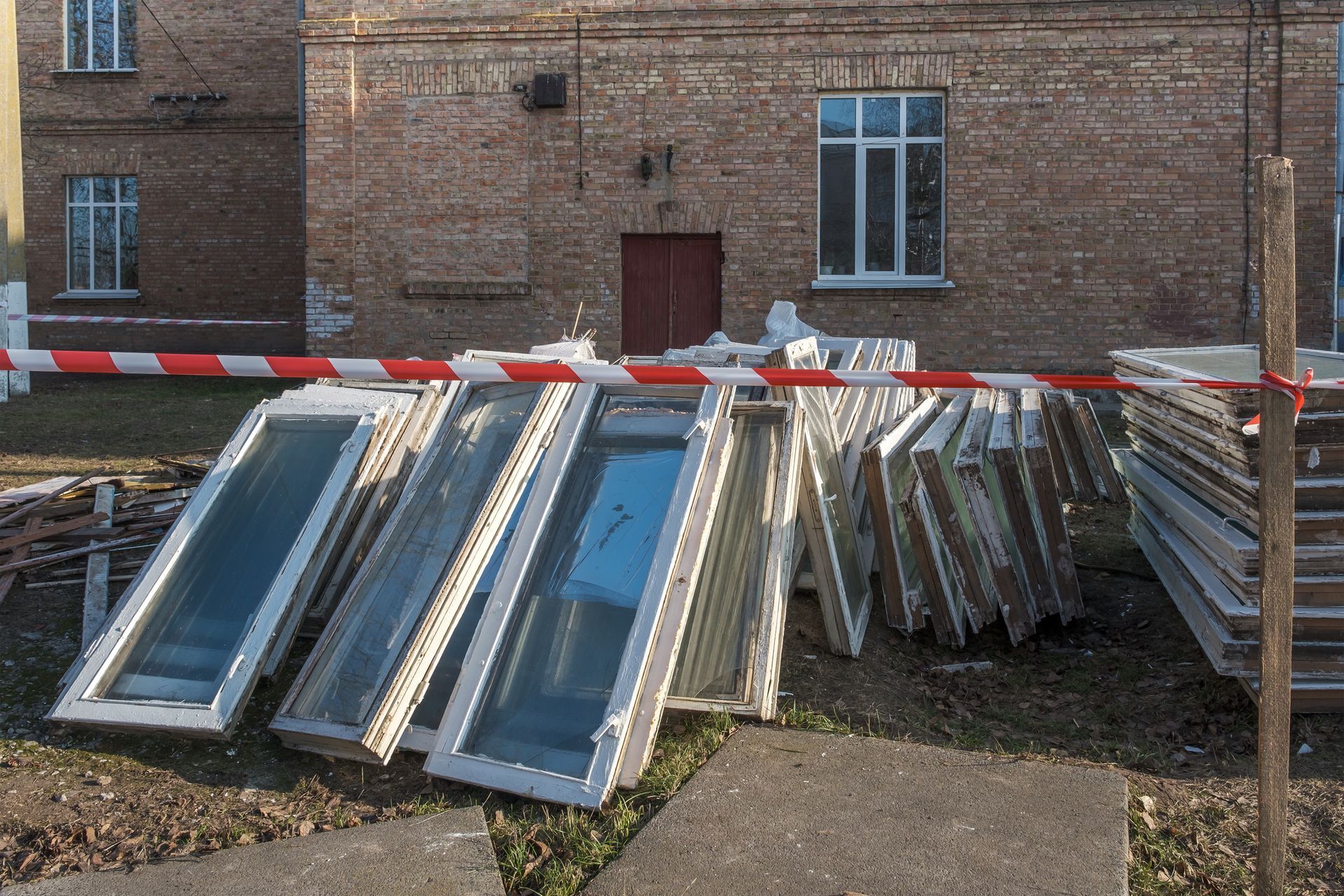 Old window frames lean against a brick building, behind red and white barrier tape.