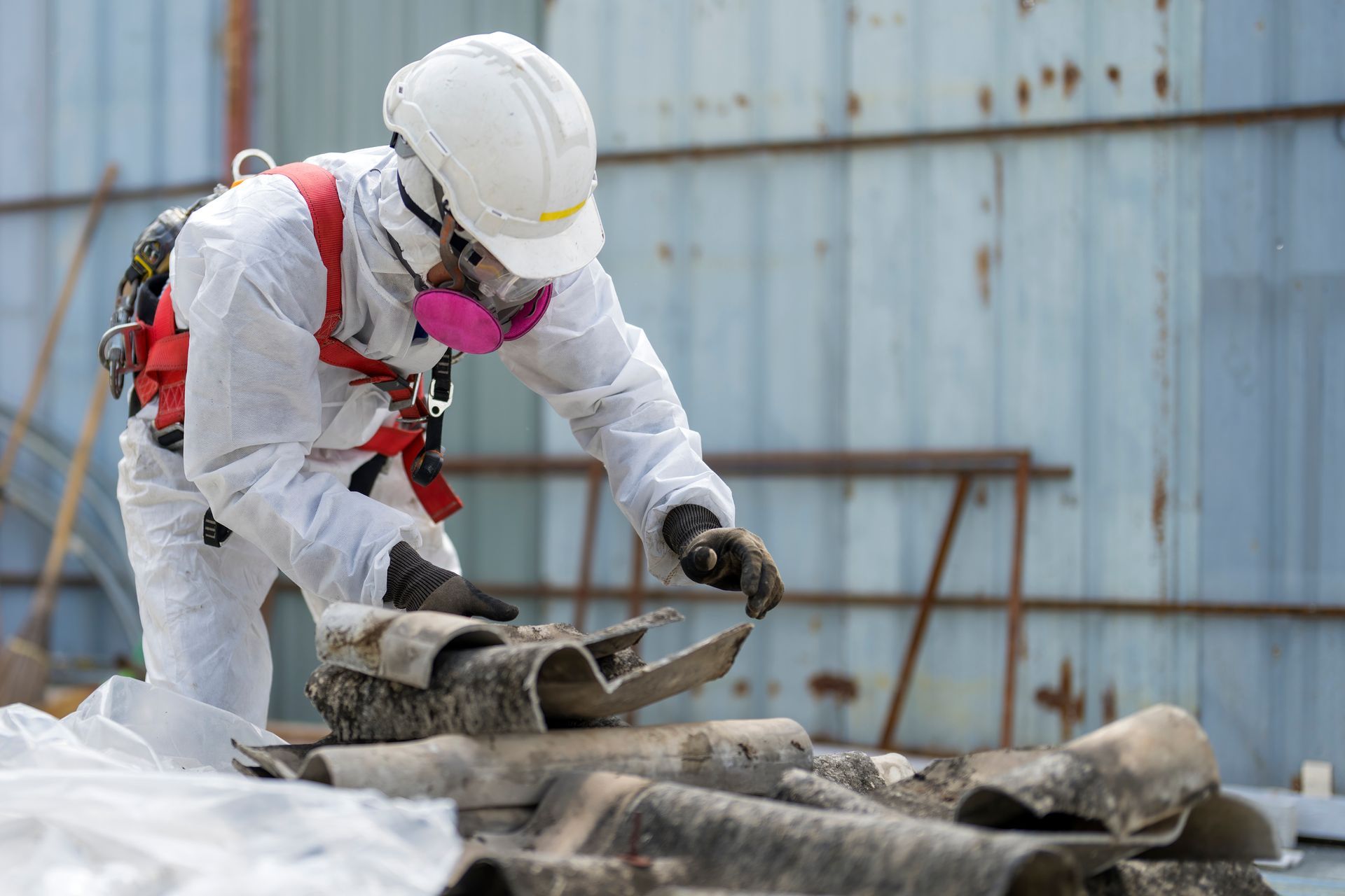 Person in protective suit examines asbestos-containing materials. Outdoors near a weathered structure.