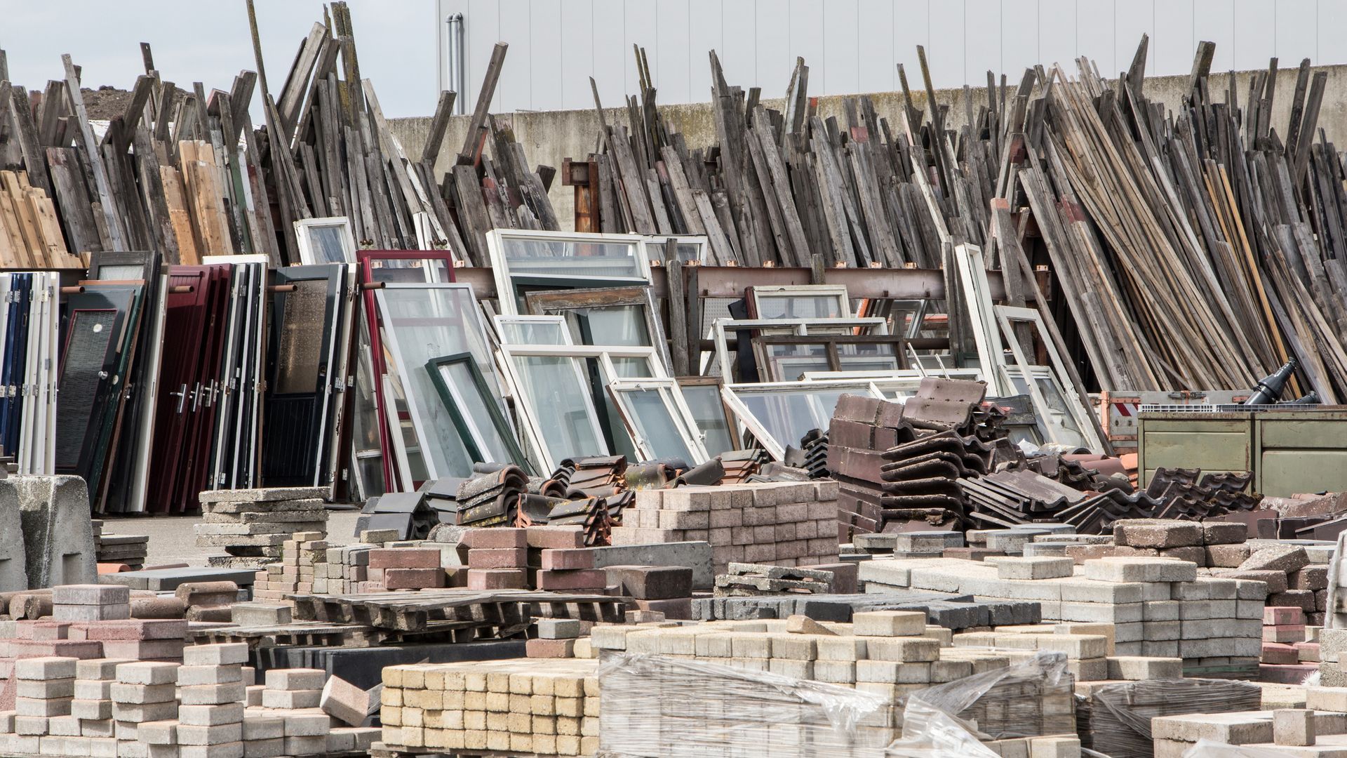 Pile of construction materials: wood planks, windows, bricks, and other debris in an outdoor storage area.