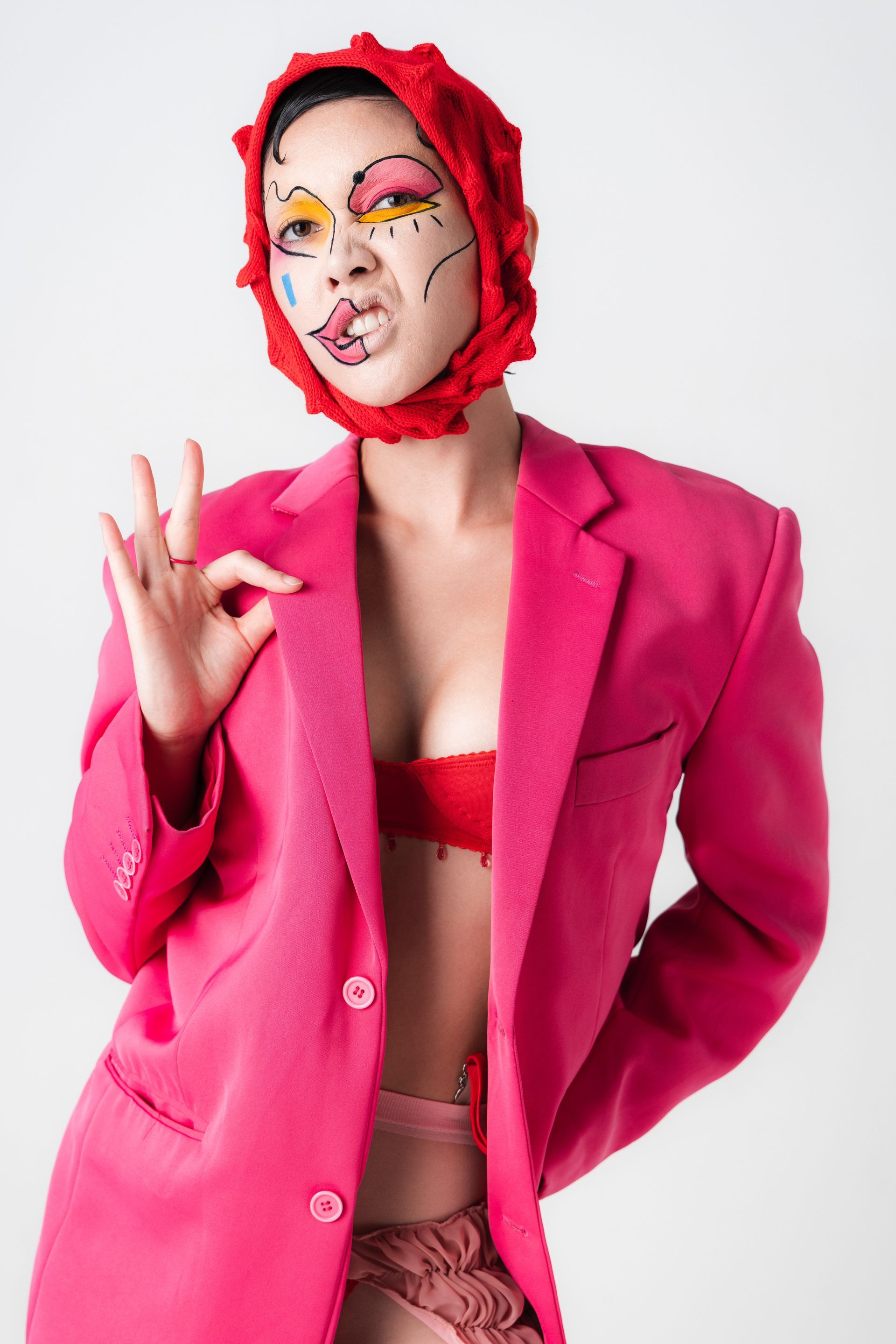 A woman wearing a pink jacket and a red hat is giving the ok sign.