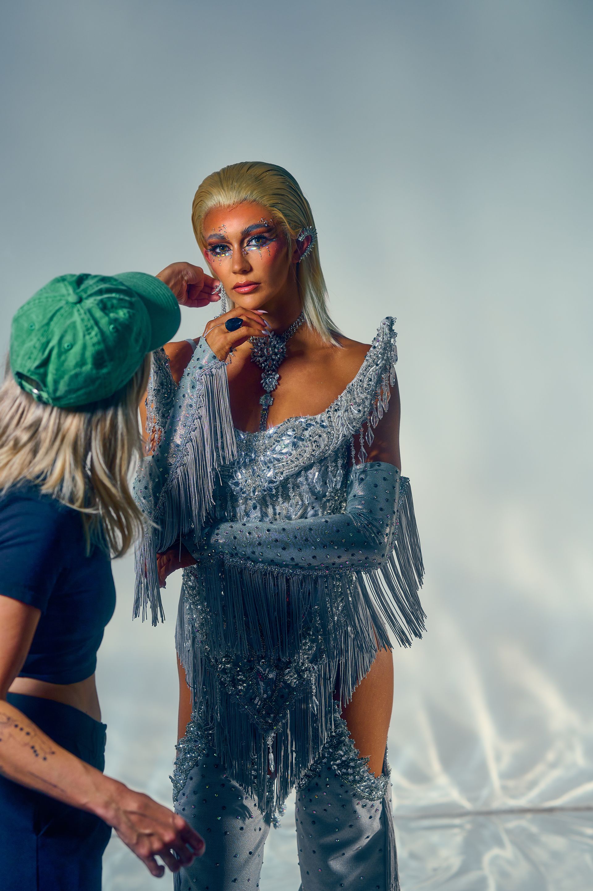 A woman in a silver dress is getting her makeup done by a makeup artist.