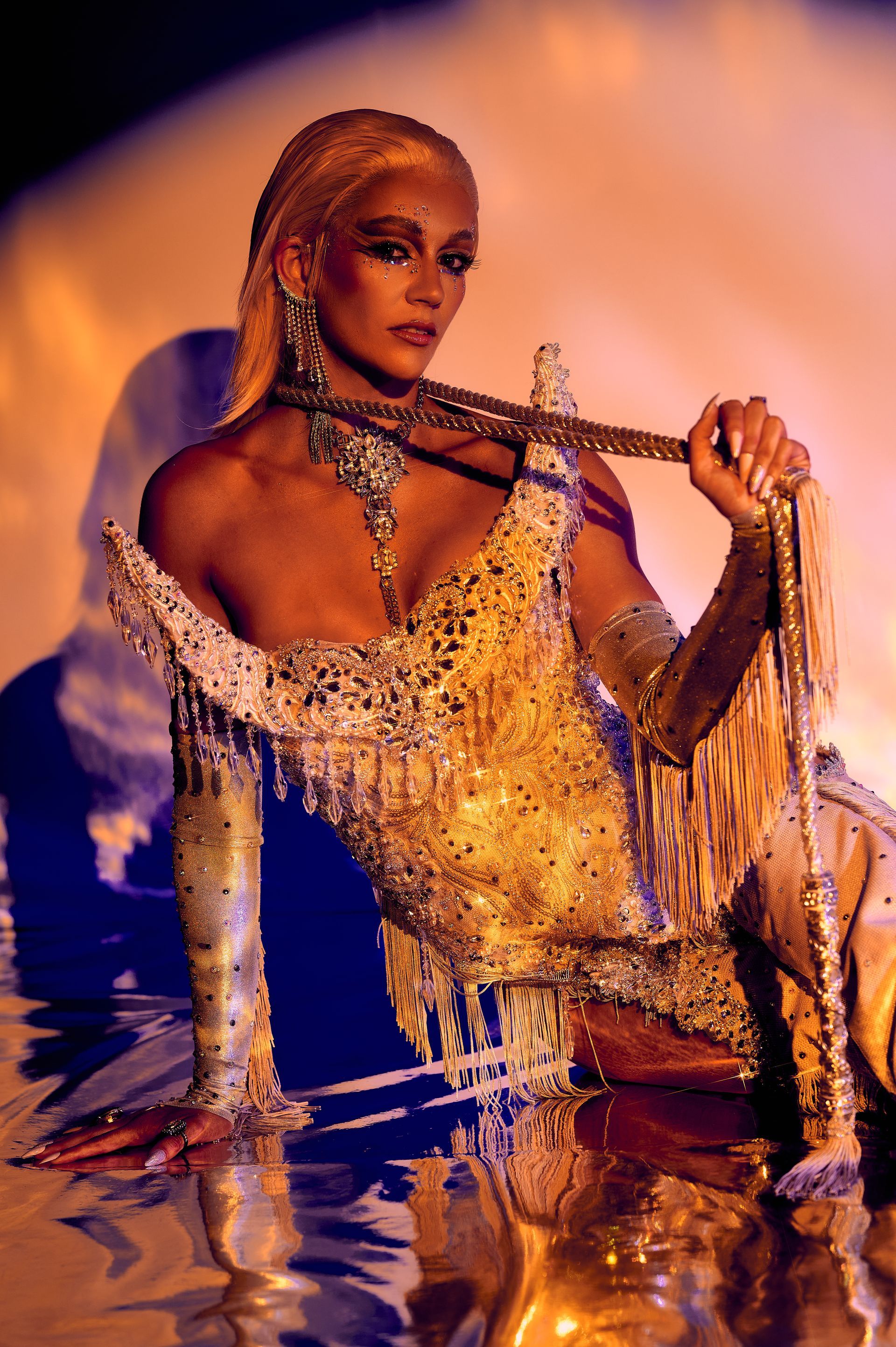 A woman in a gold dress is sitting on a table holding a necklace.