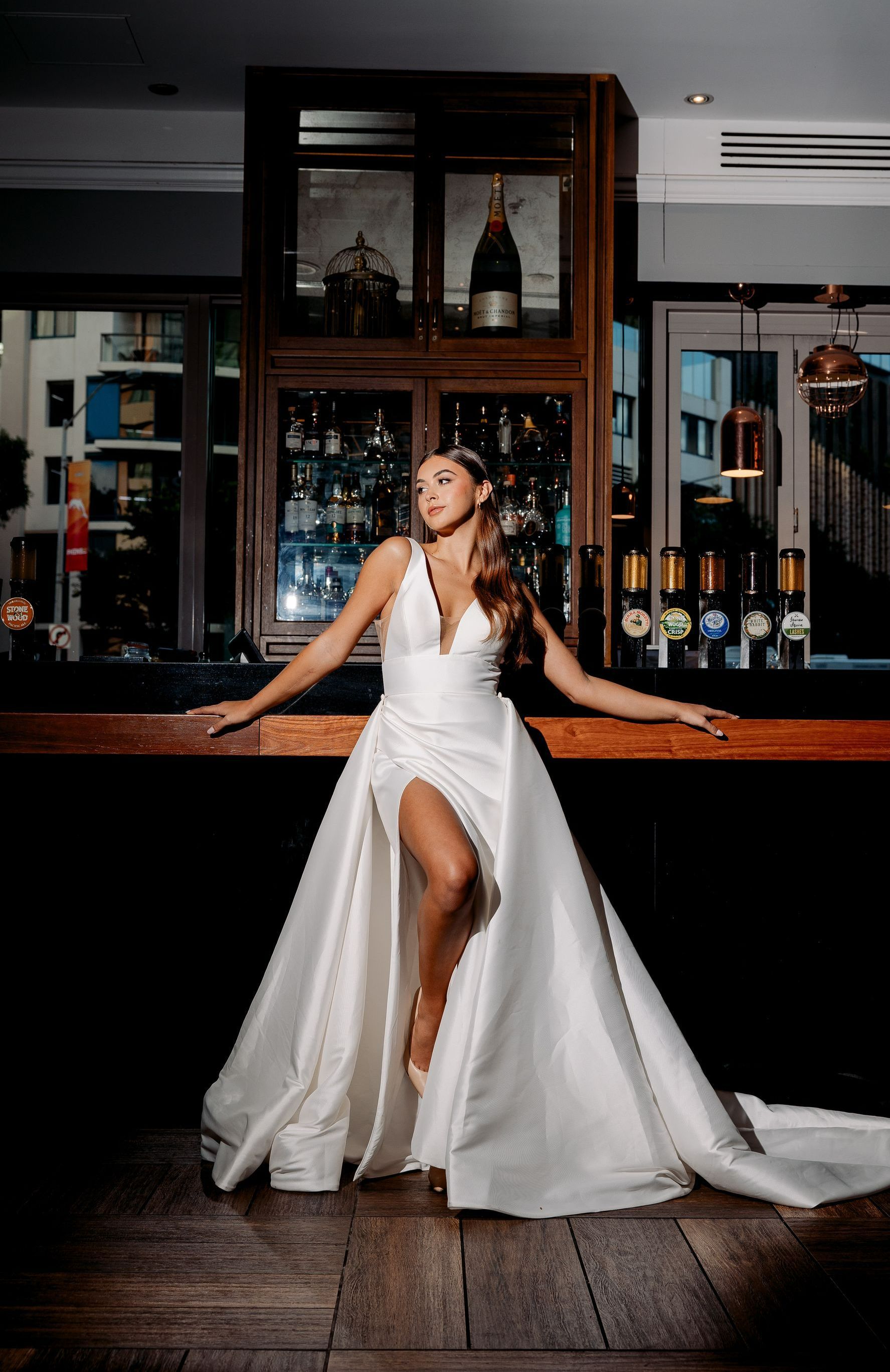 A woman in a wedding dress is leaning on a bar.