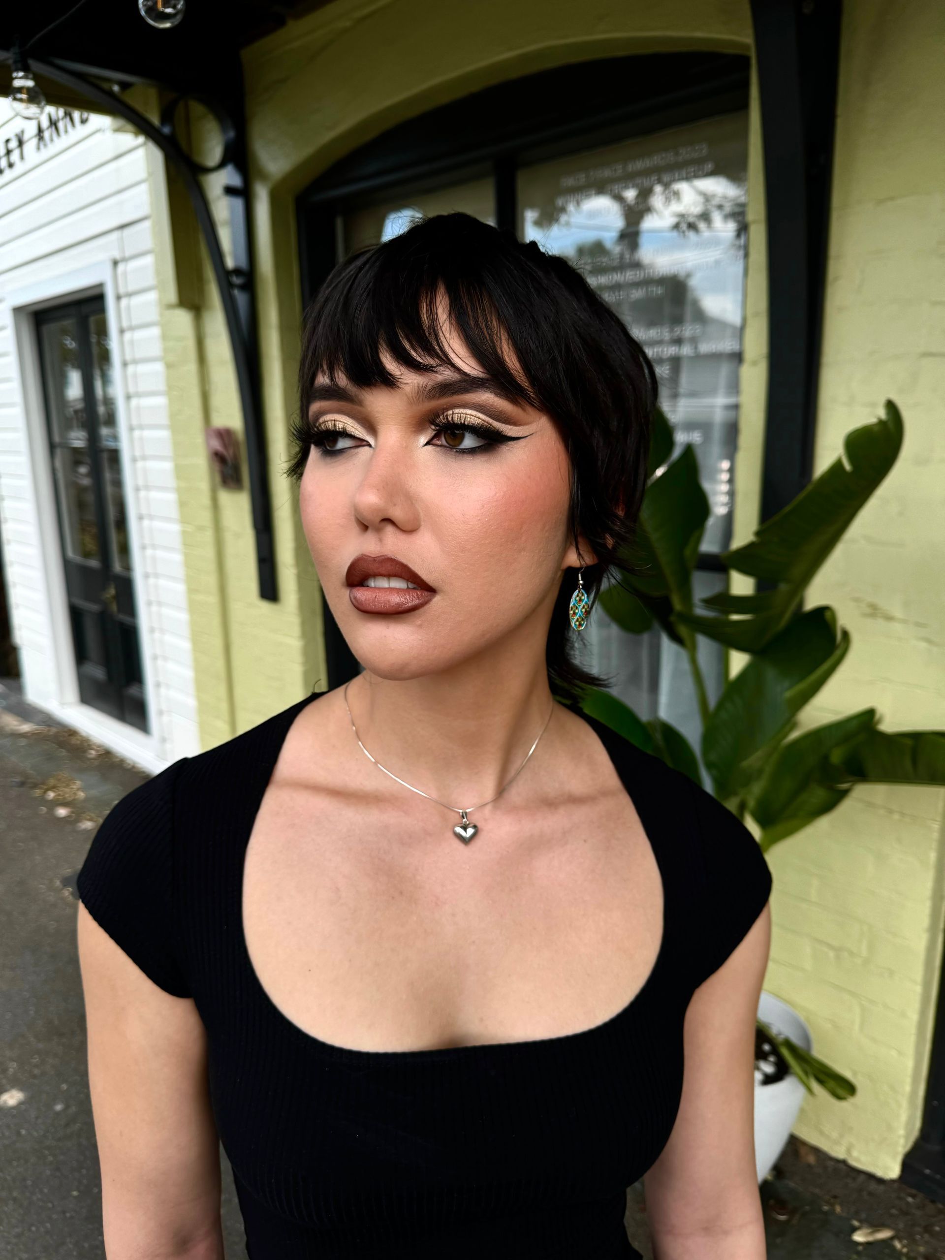 A woman wearing a black top and a necklace is standing in front of a building