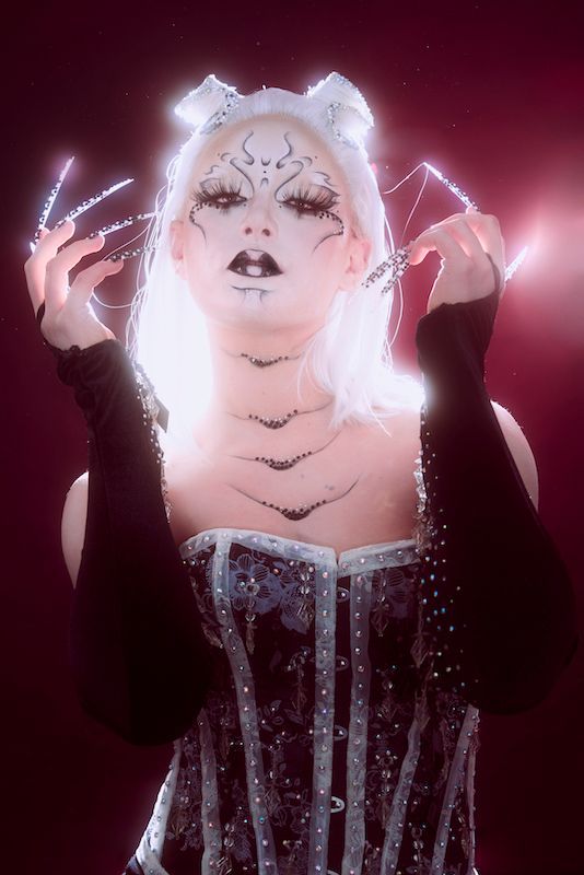 A woman with white hair is wearing a black corset and black gloves.