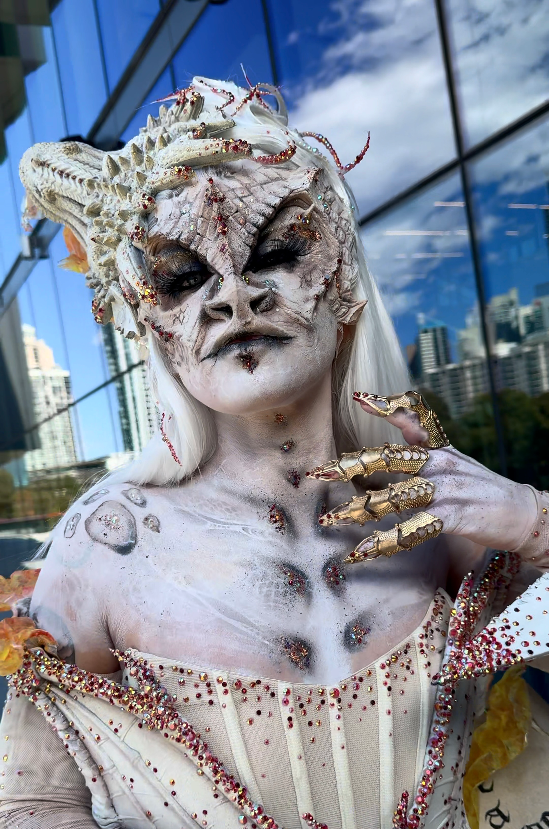 A woman in a costume with a snake on her hand is standing in front of a building.