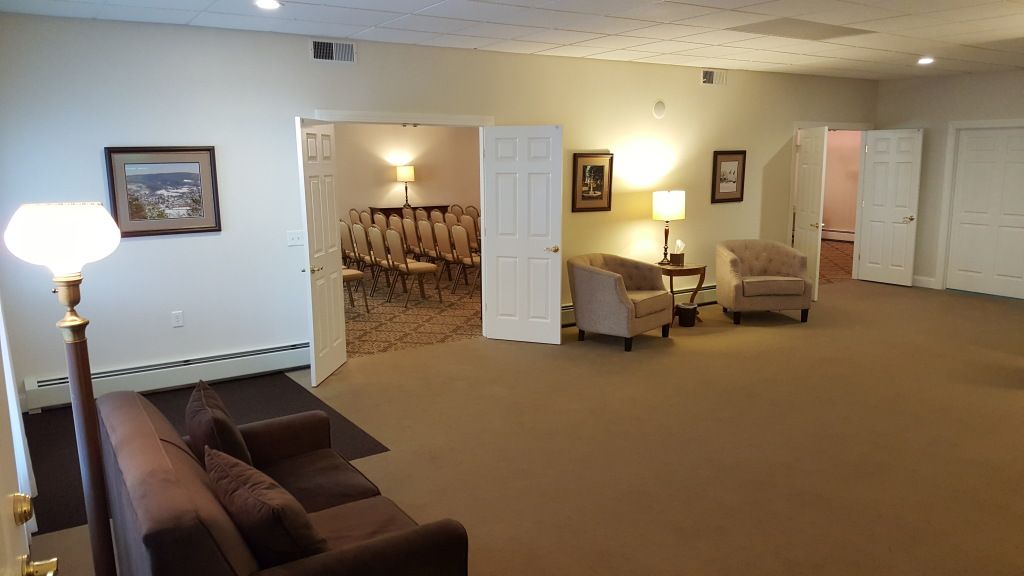 Interior of a funeral home with open doors leading to a chapel, seating area with chairs and a sofa.