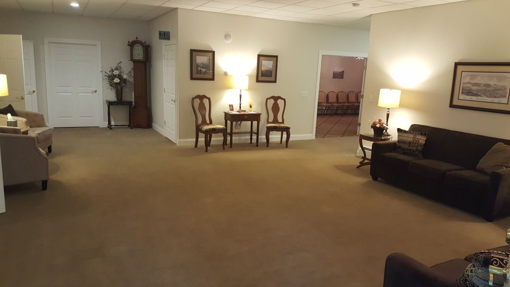 Interior view of a funeral home waiting area with furniture, lamps, and a grandfather clock.
