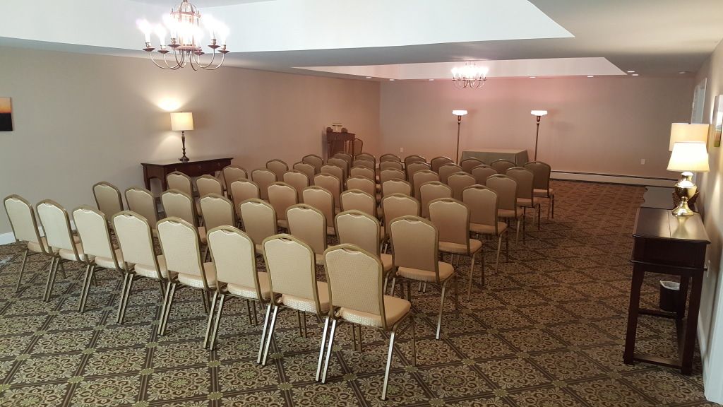 Empty room with beige chairs arranged for an event. The room has neutral walls, patterned carpet, and chandeliers.