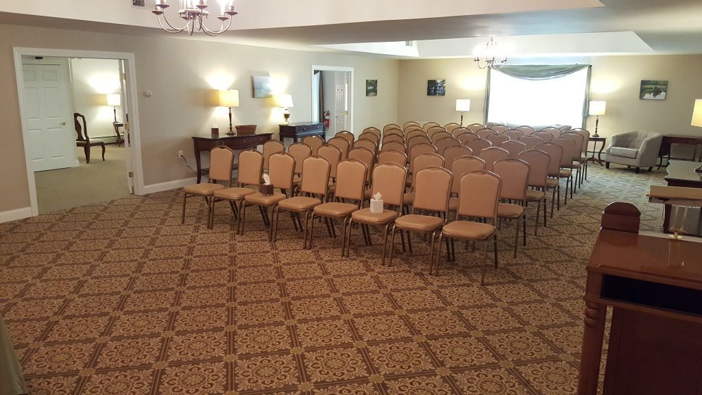 Rows of chairs set up in a large room, likely for a gathering. Beige carpet, neutral walls, and a few lamps visible.