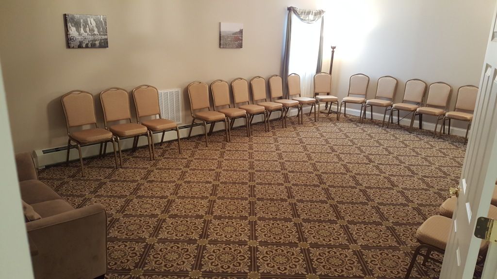 Empty room with tan chairs arranged in a circle on patterned carpet.
