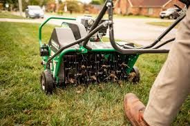 A person operating a green lawn aerator, on grass.