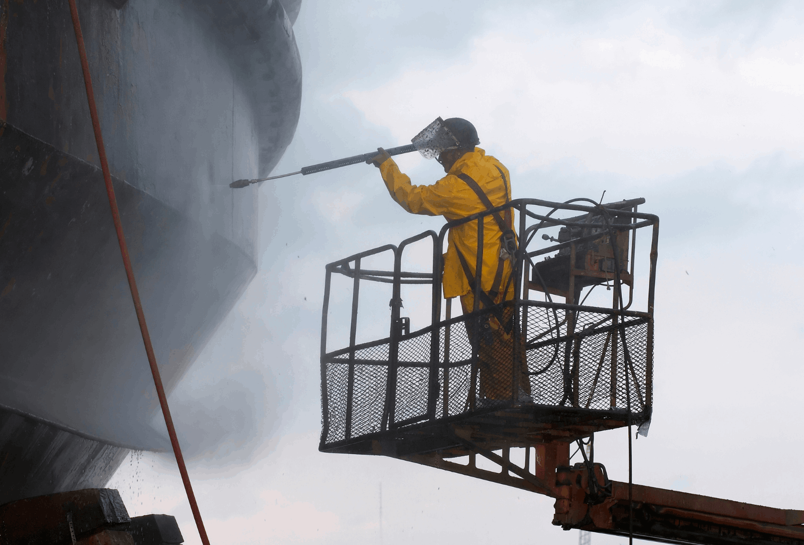 Man standing on platform cleaning silo with pressure washing equipment