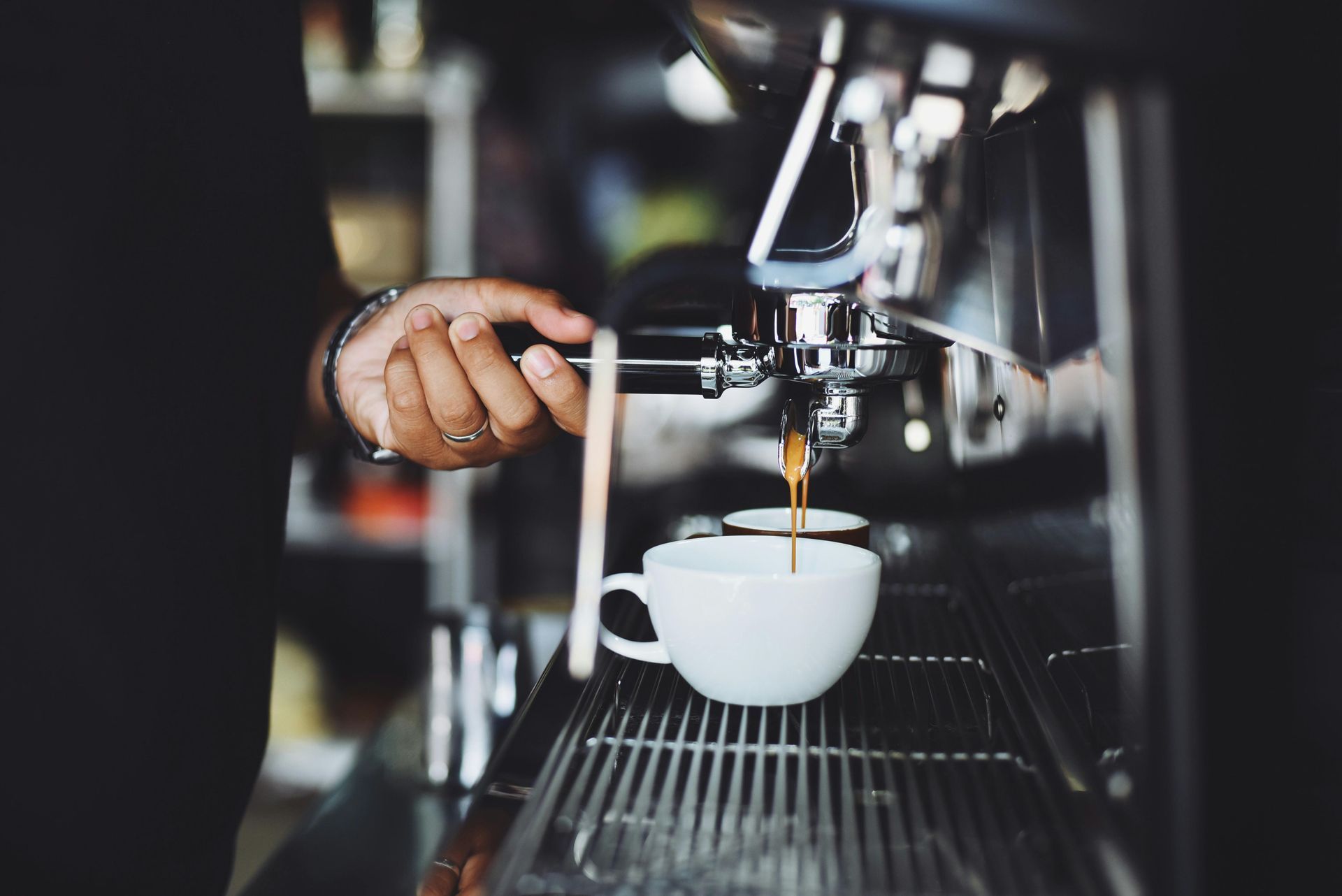 Person making espresso, pouring coffee into a white cup from a machine in a cafe.