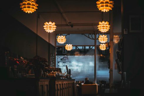 Dimly lit cafe interior with hanging flower-shaped lights. A blurry figure sits by the window.