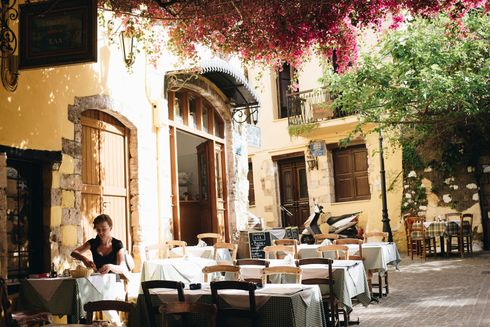 Outdoor cafe, woman setting a table, checkered tablecloths, flowers overhead, sunny day.