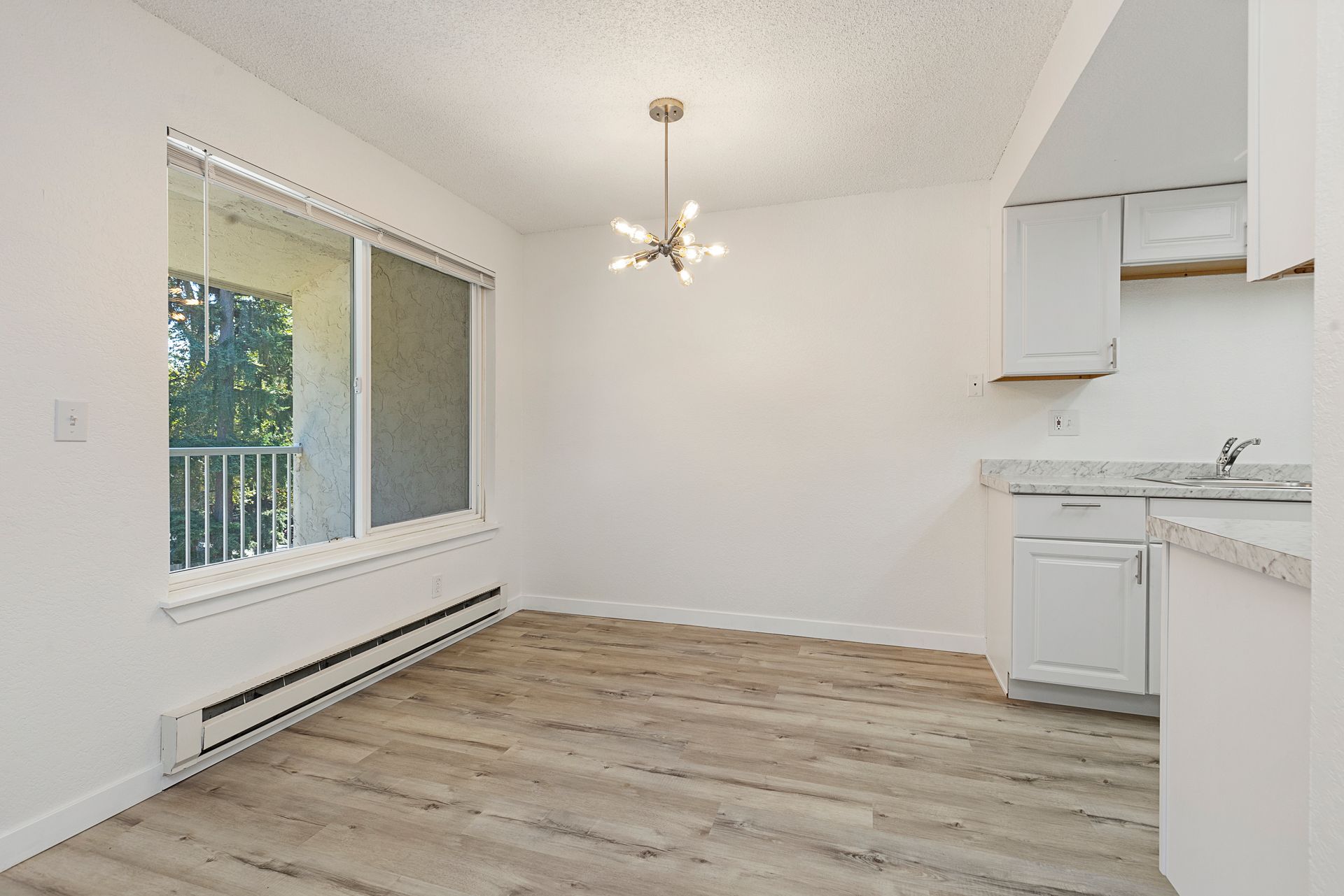 an empty dining room with a large window and a kitchen .