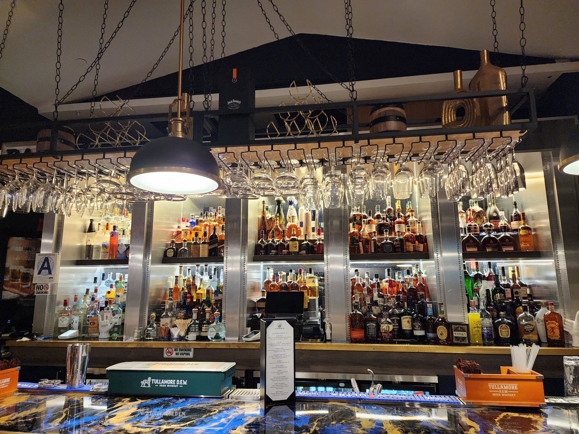 A bar with a lot of bottles of alcohol and wine glasses hanging from the ceiling.
