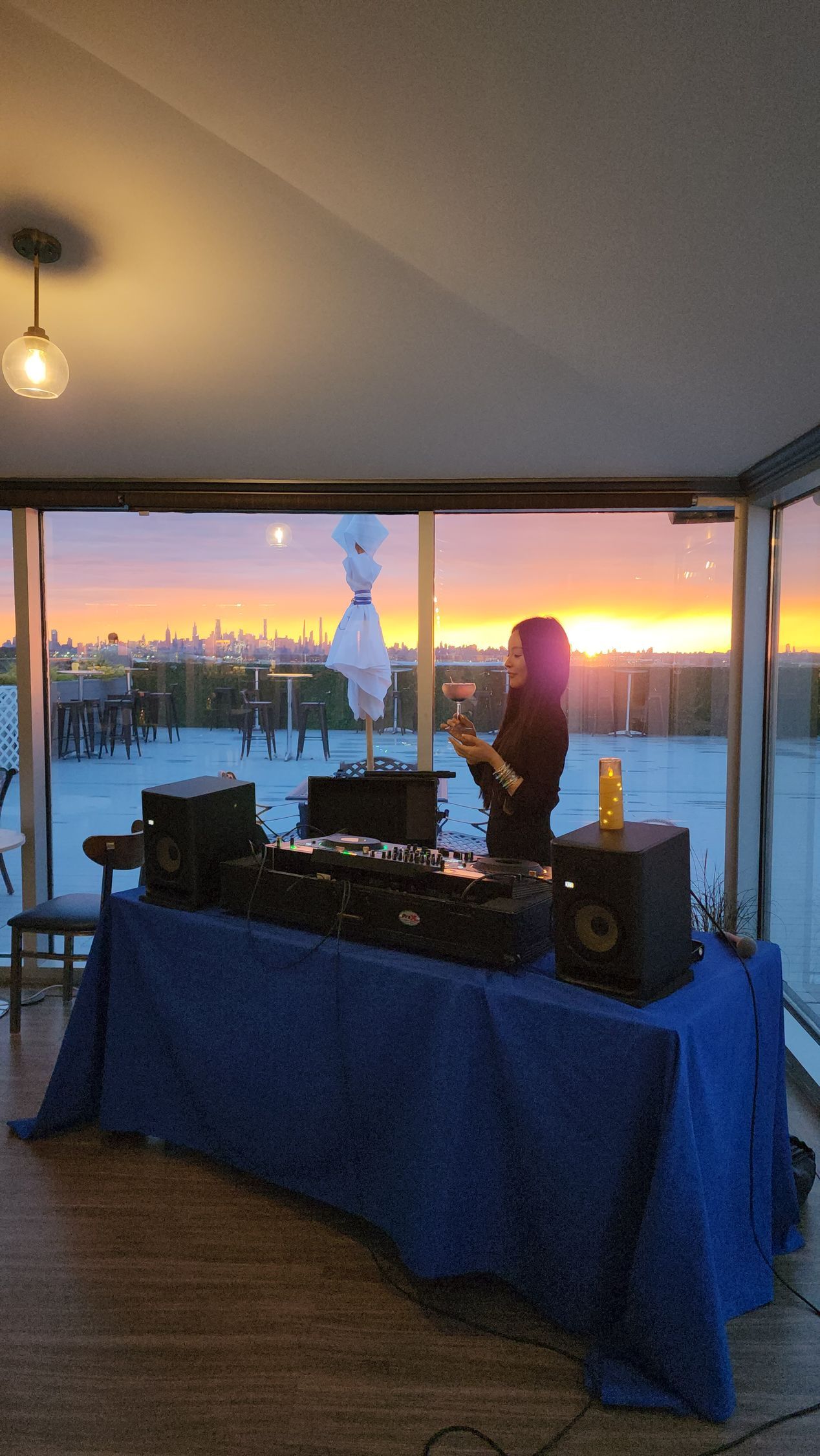 A woman is standing in front of a table with speakers and a sunset in the background.