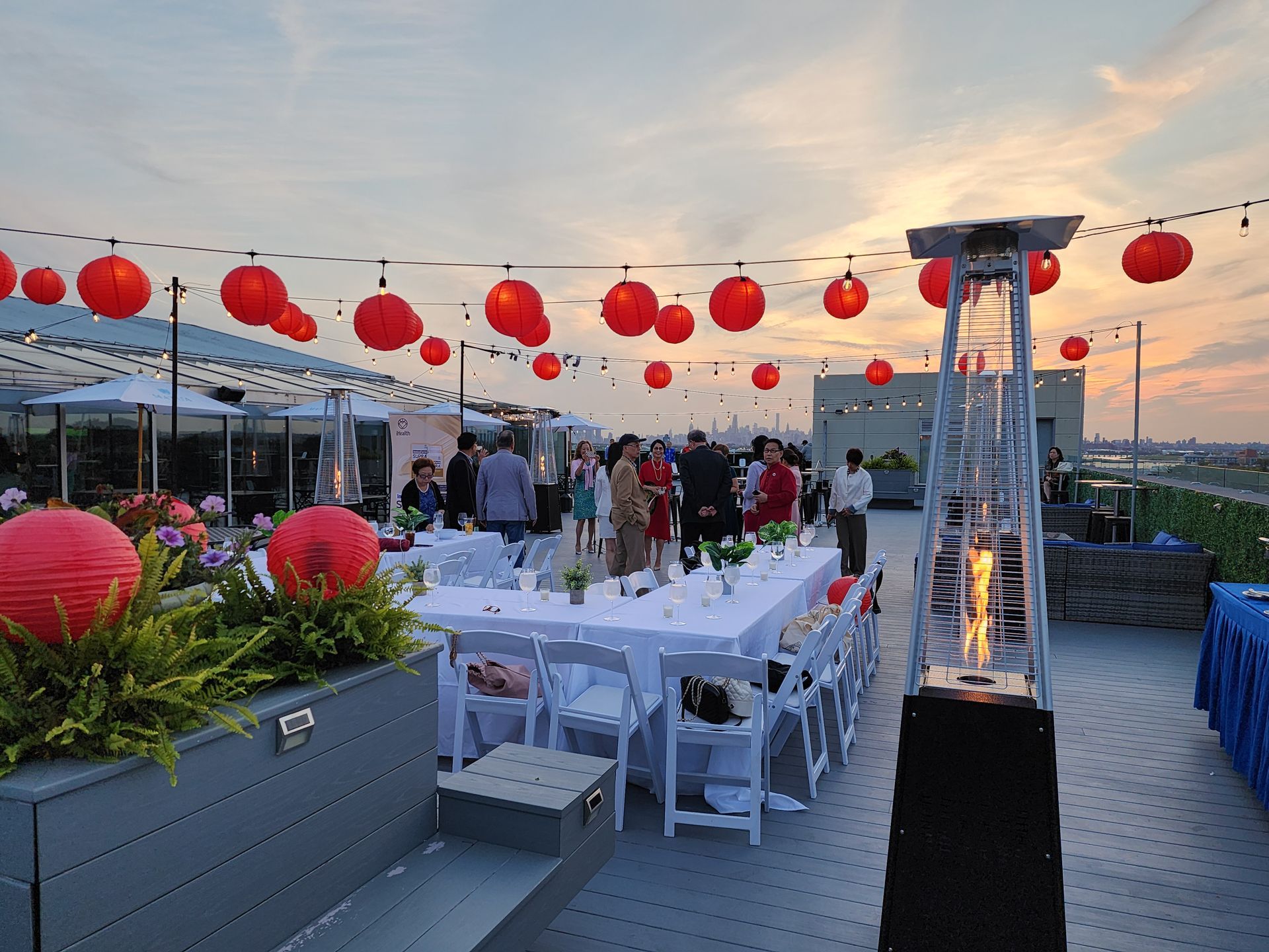 A group of people are standing around tables and chairs on a rooftop.