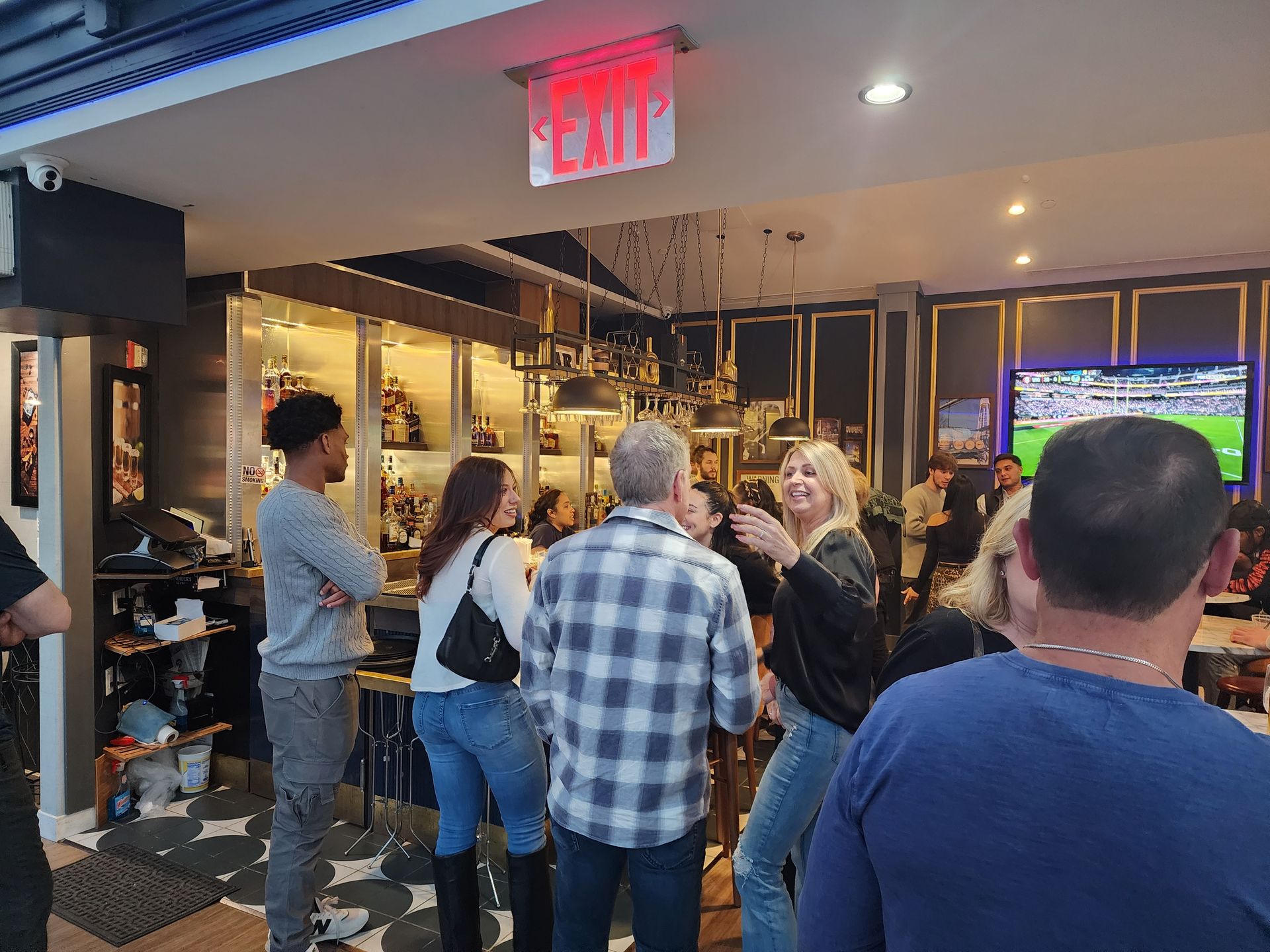 A group of people are standing in a room with a red exit sign.