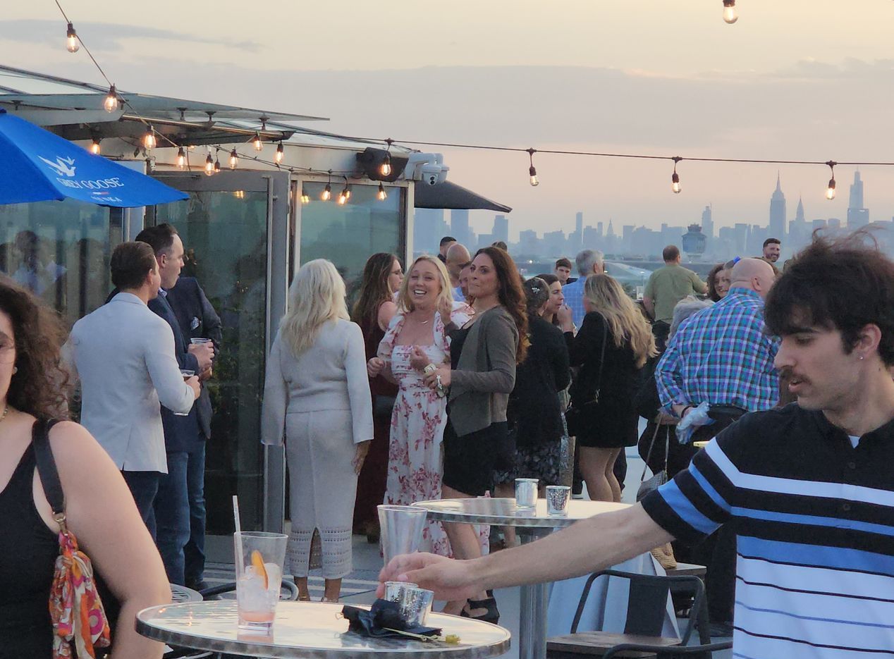 A group of people are standing around tables with a blue umbrella in the background