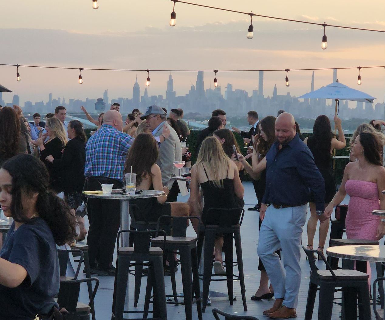 A large group of people are gathered around tables and stools