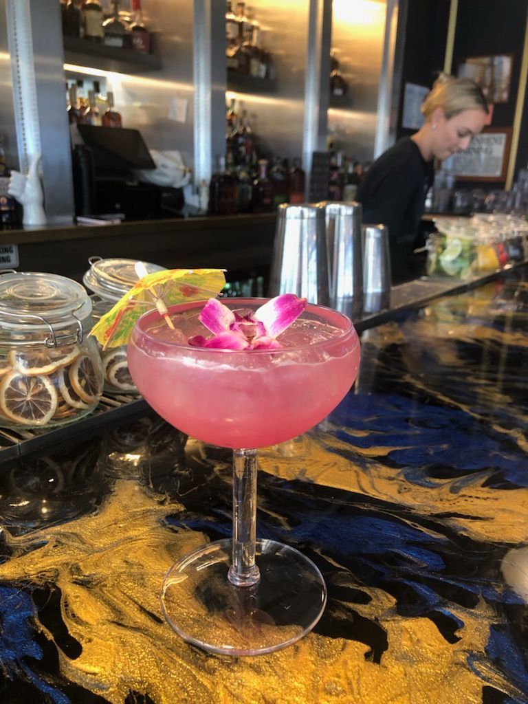 A pink cocktail with flowers in it is sitting on a bar.