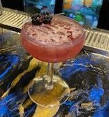 A close up of a cocktail in a martini glass on a bar.