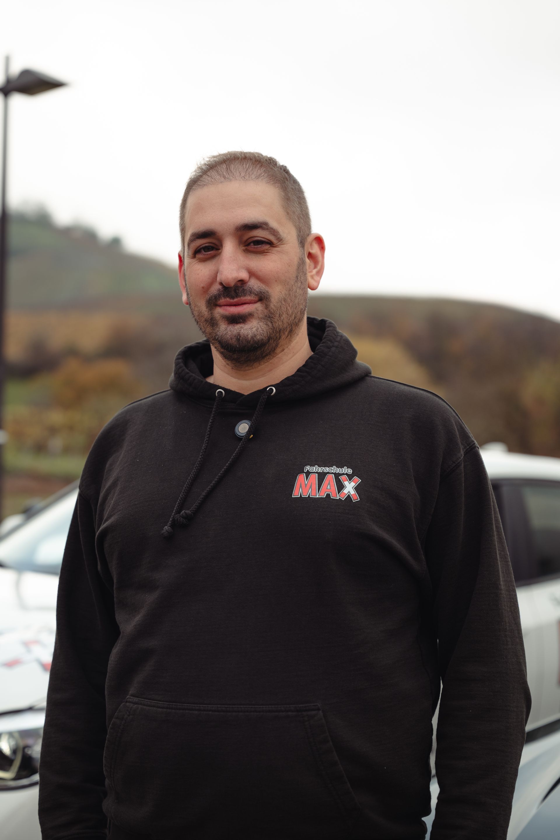 Ein Mann mit einem schwarzen Kapuzenpullover steht vor einem Auto.