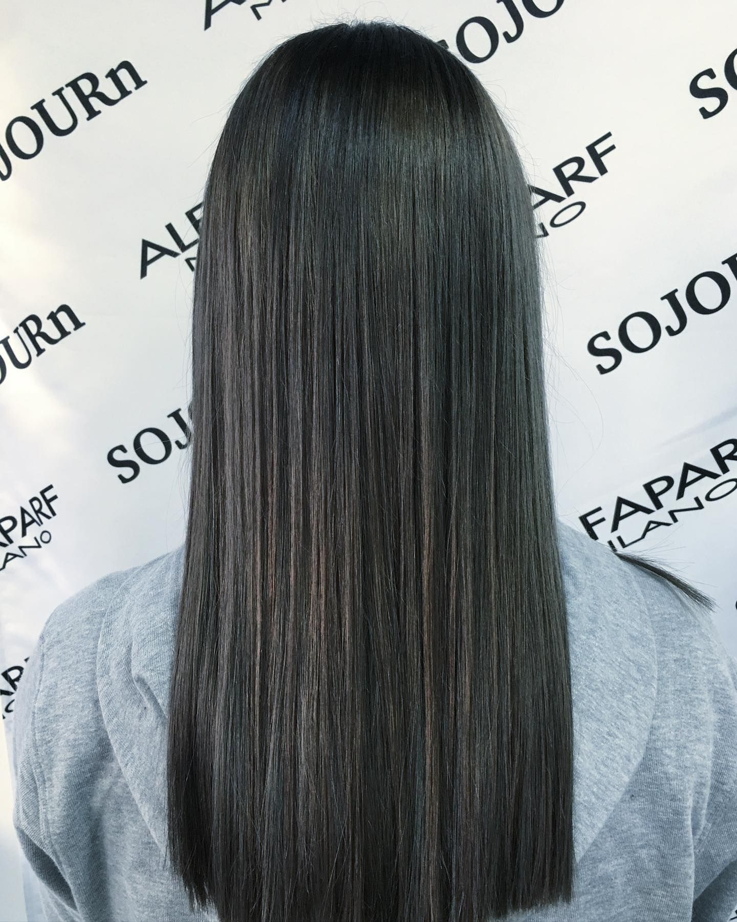 A woman with long black hair is standing in front of a sign that says sojourn