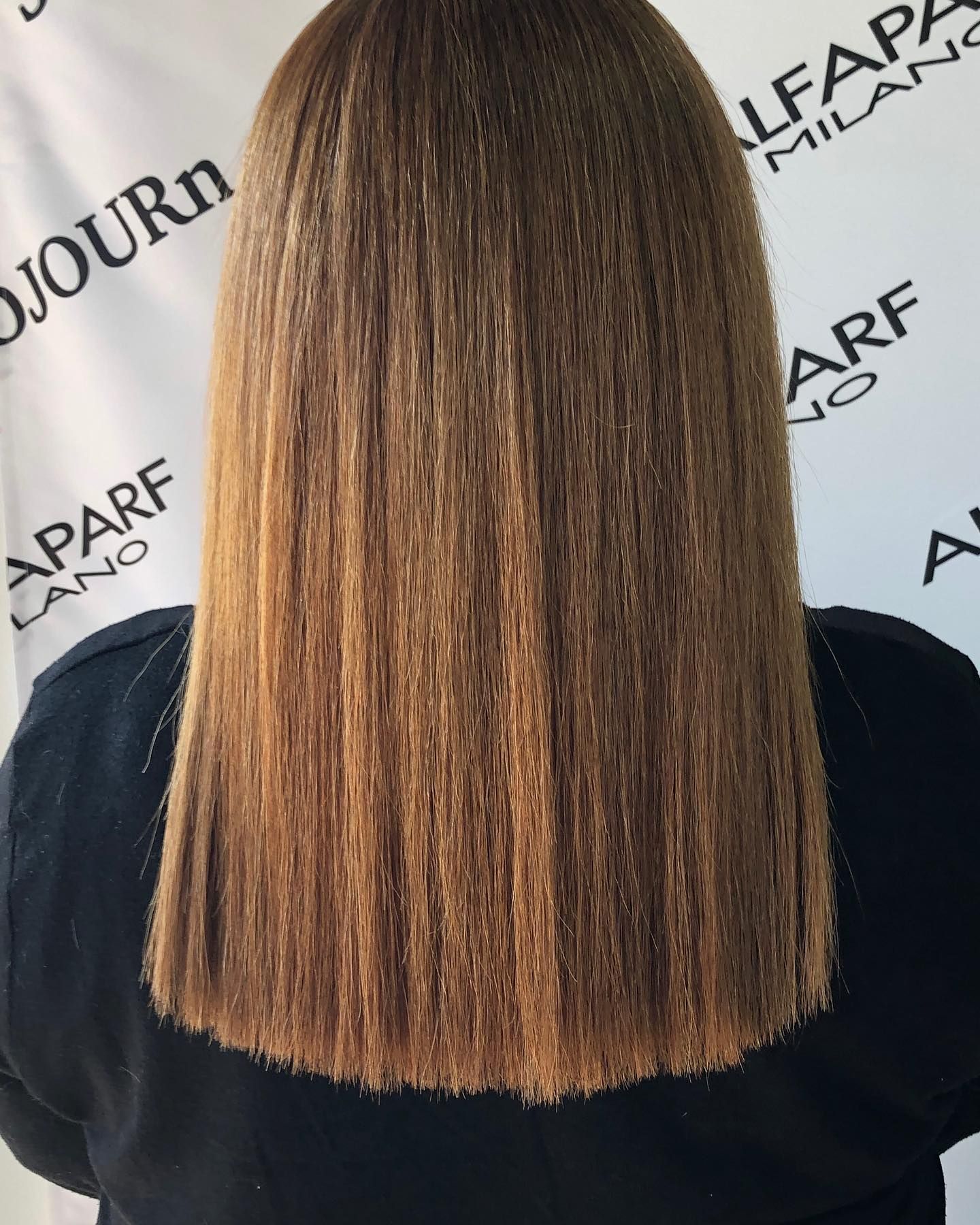 A woman with long brown hair is standing in front of a sign that says milano