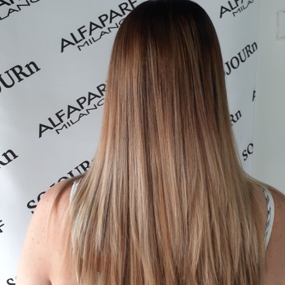 A woman is standing in front of a wall that says alfaparf milano