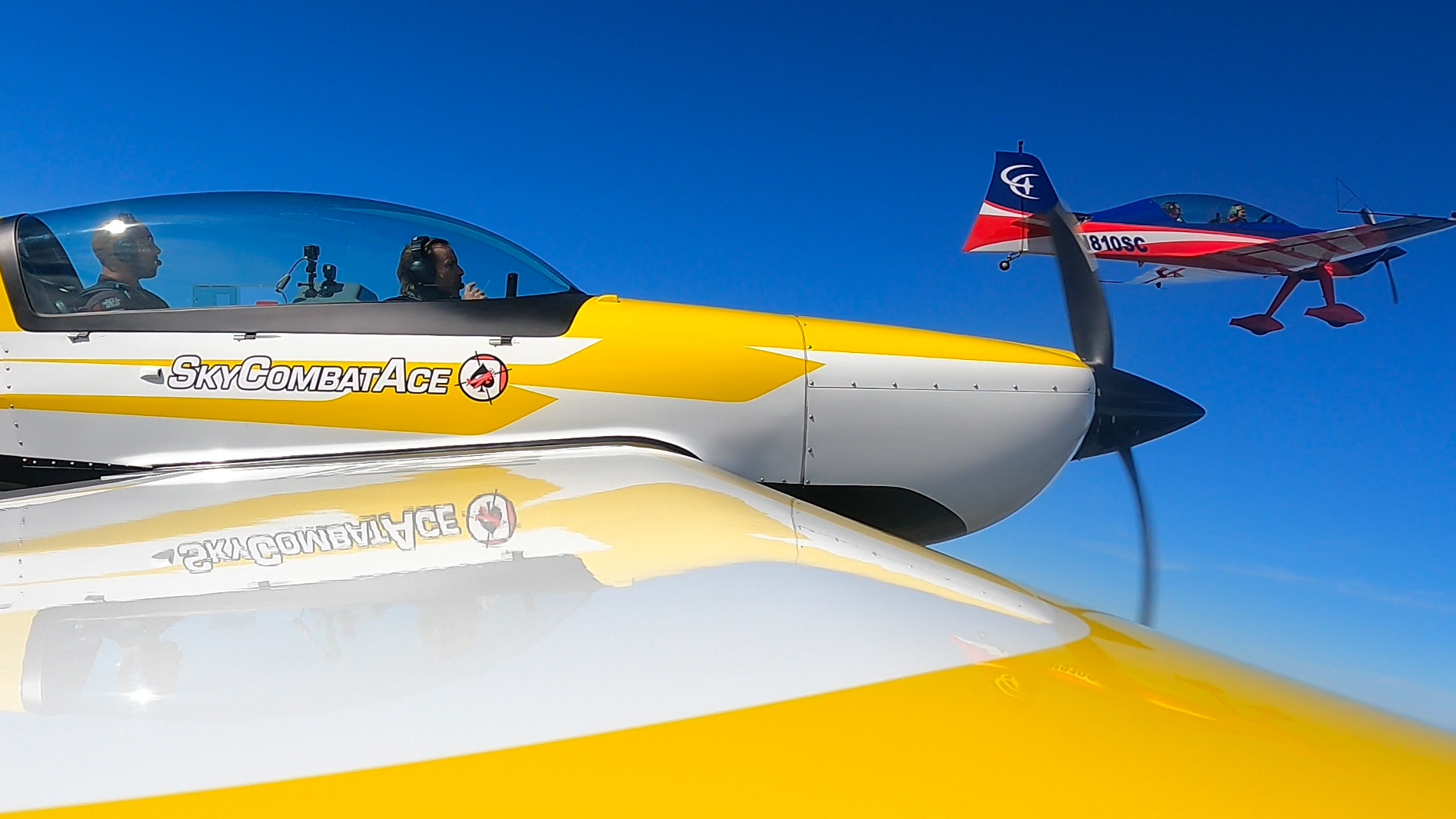 A yellow and white plane is flying in the sky next to another plane.