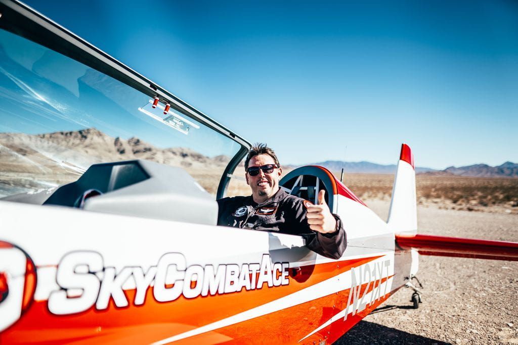 A pilot smiling and giving a thumbs up while sitting in a Sky Combat Ace plane. 