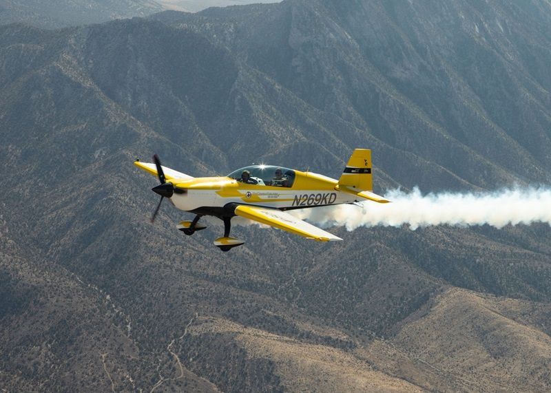 A yellow Sky Combat Ace plane flying near mountains. 