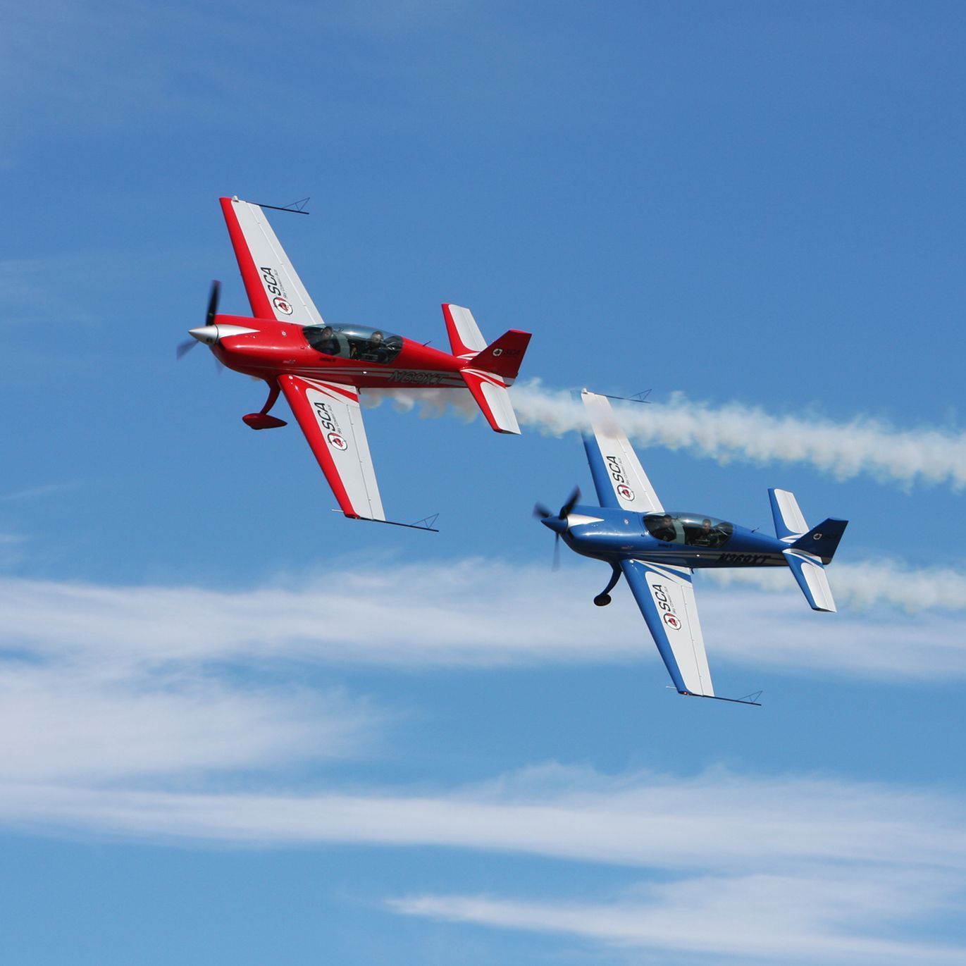 Two red and blue airplanes are flying side by side in the sky