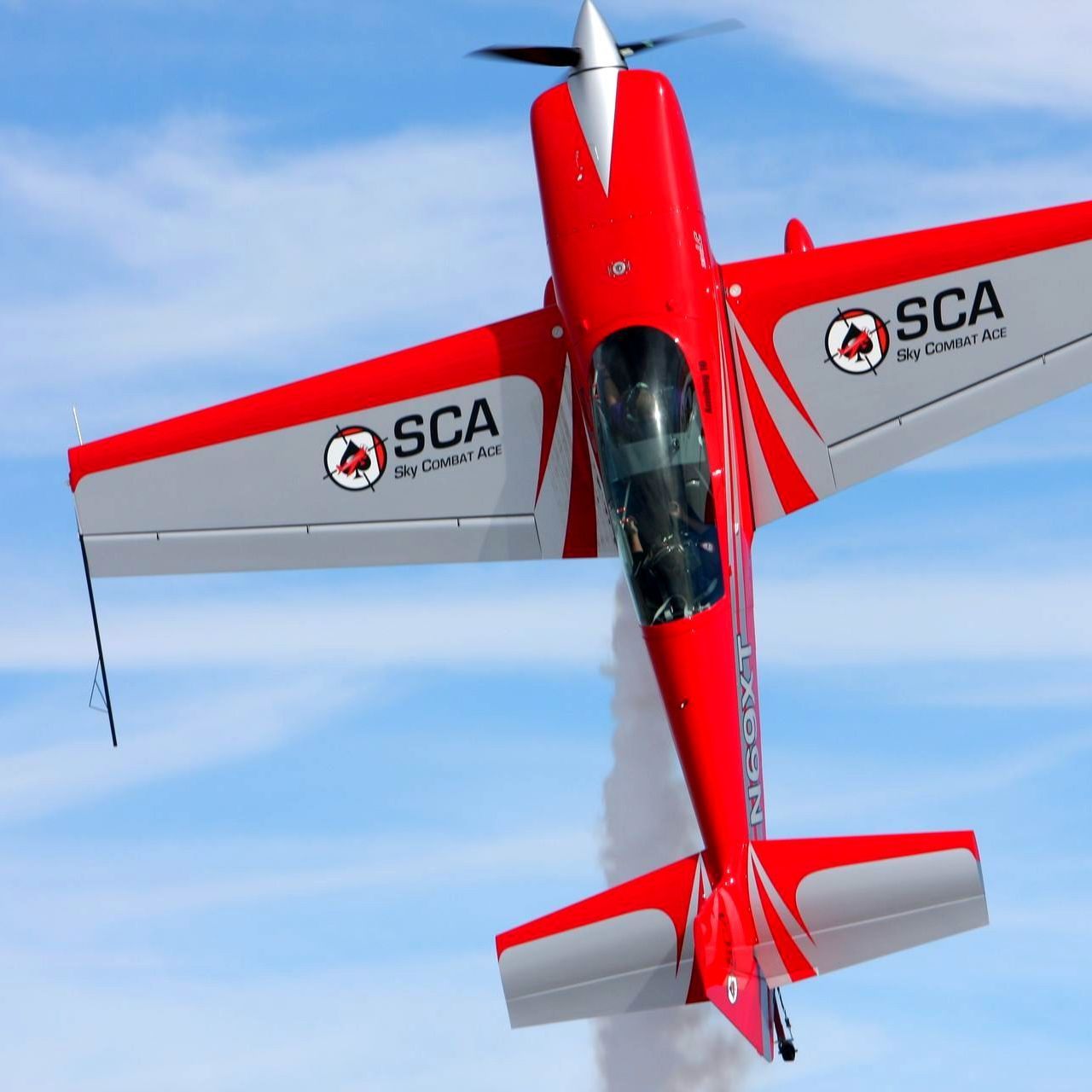 A red and gray airplane with sca on the wings is flying in the sky