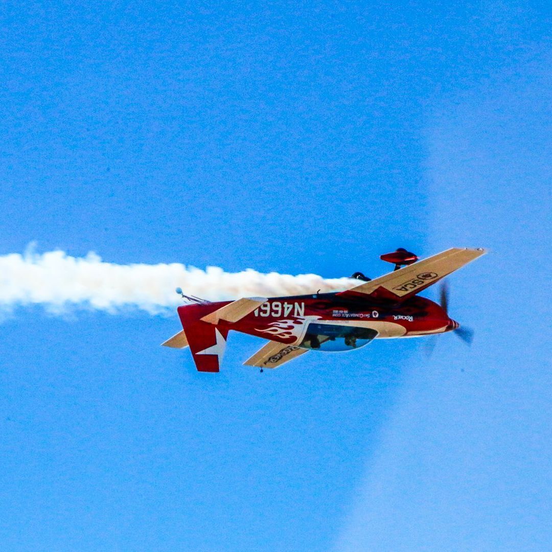 A red airplane is flying in a blue sky with smoke coming out of it