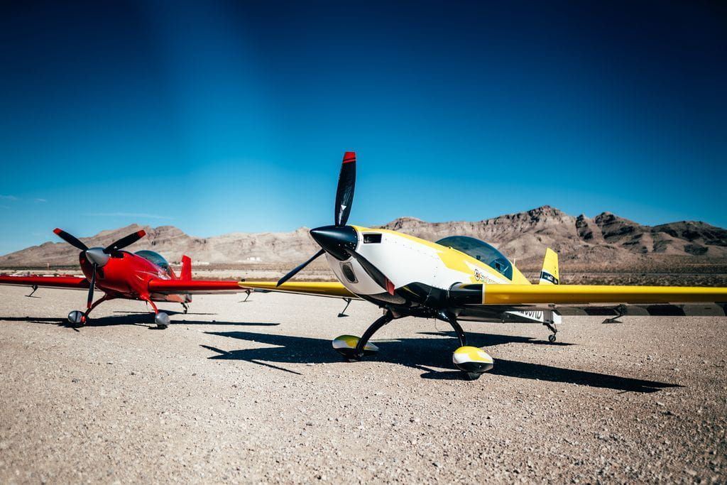 Two Sky Combat Ace planes, one red one yellow, sit next to each other in the desert. 