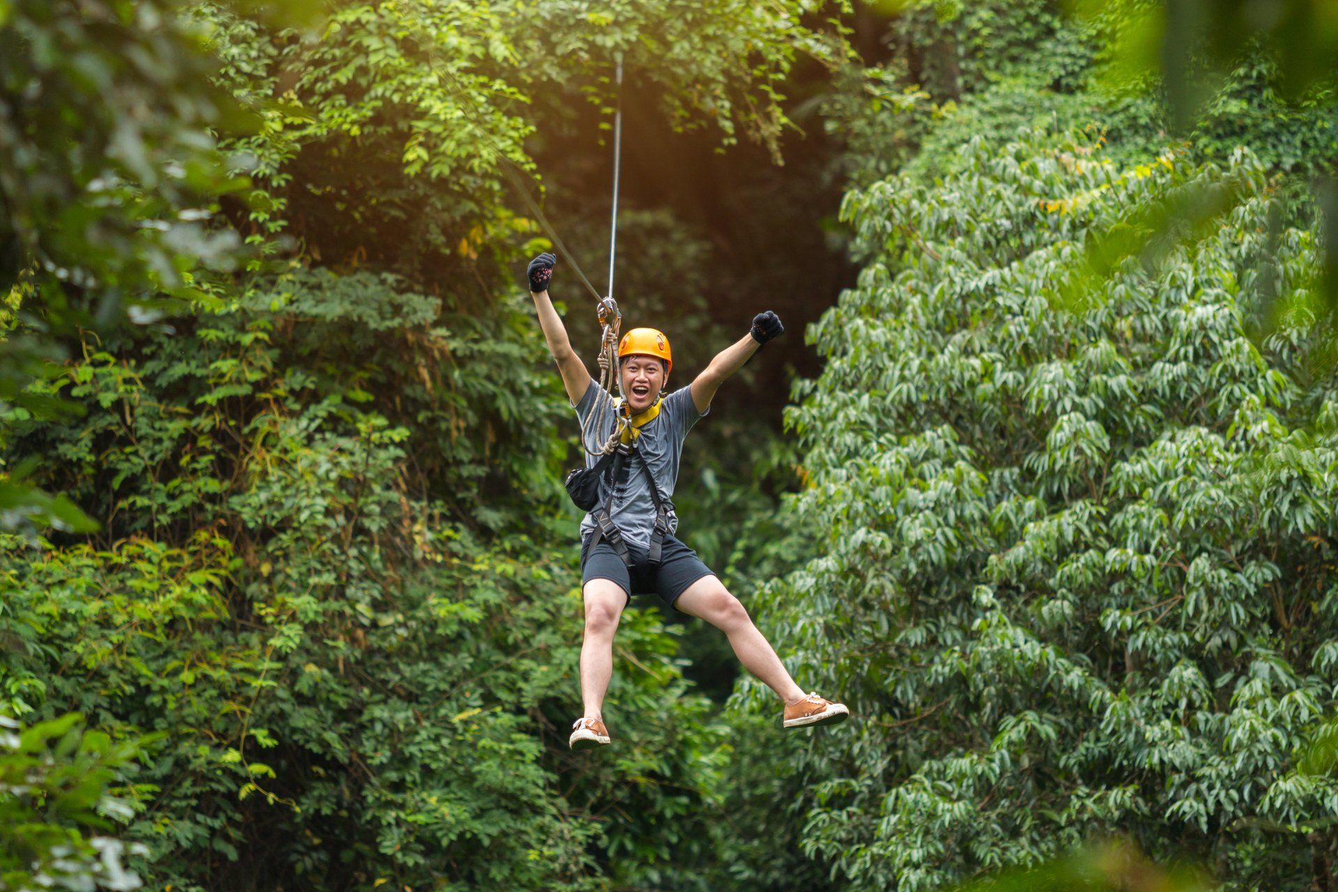 adrenaline junkie zip lining with his hands in the air and screaming of excitement