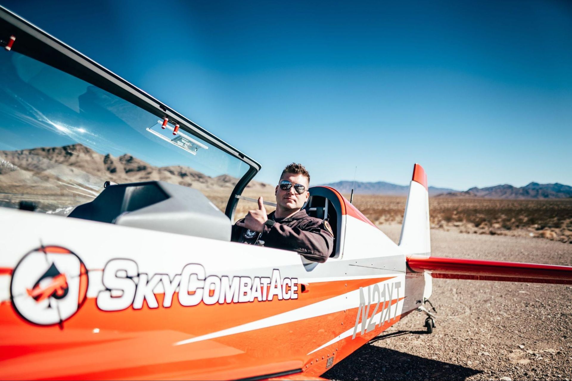 A pilot giving the thumbs up while sitting in a Sky Combat Ace plane, a San Diego outdoor activity.