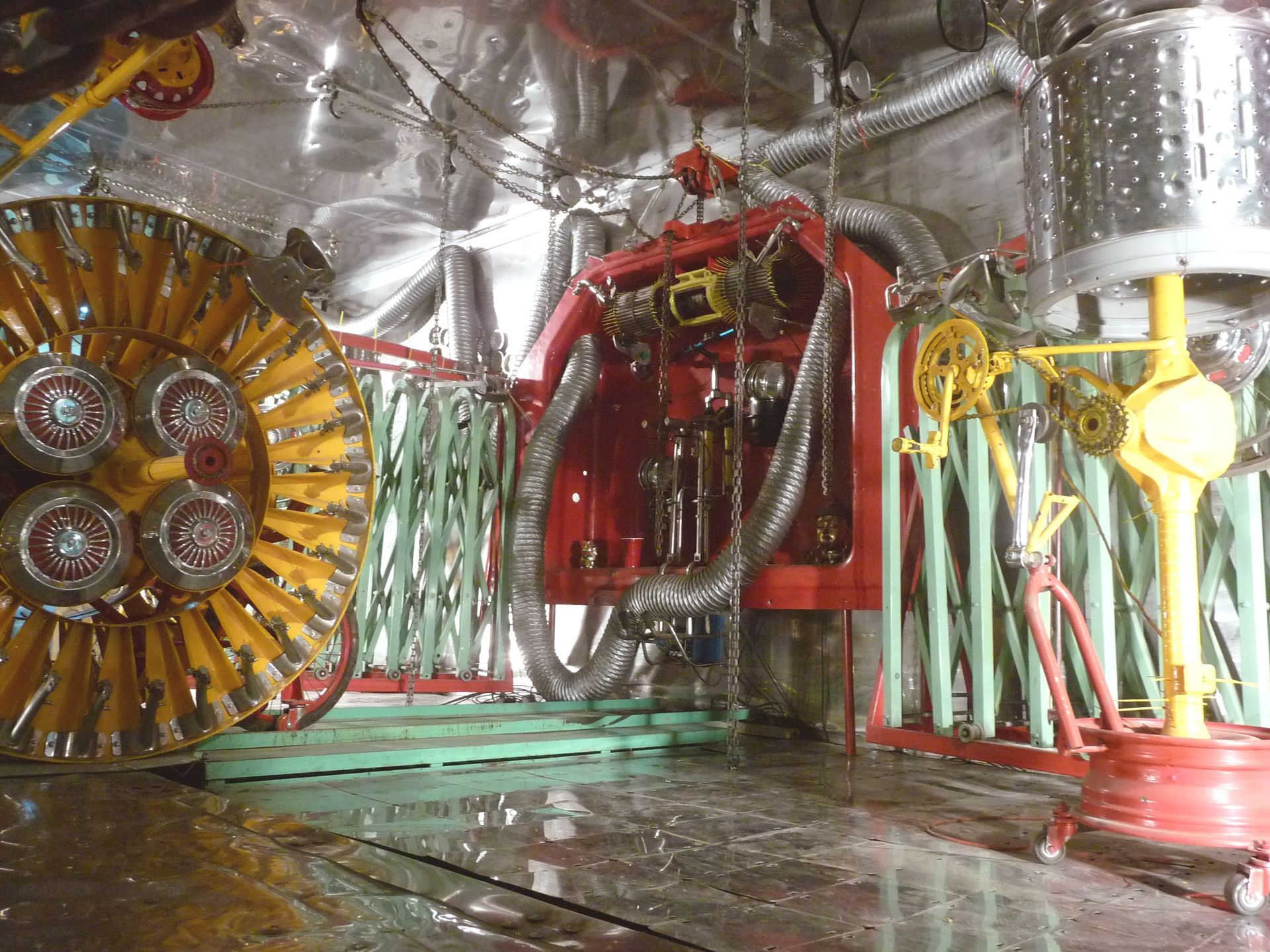 Inside a shiny metal chamber, complex red and yellow machinery with many pipes and cylindrical components.