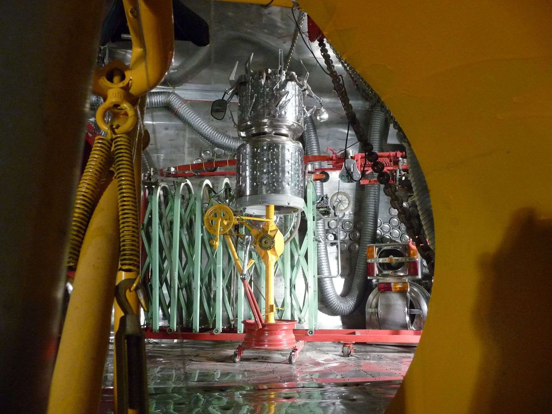 Interior view of machinery, with a central vertical metal structure, green tubes, and yellow frame partially visible.
