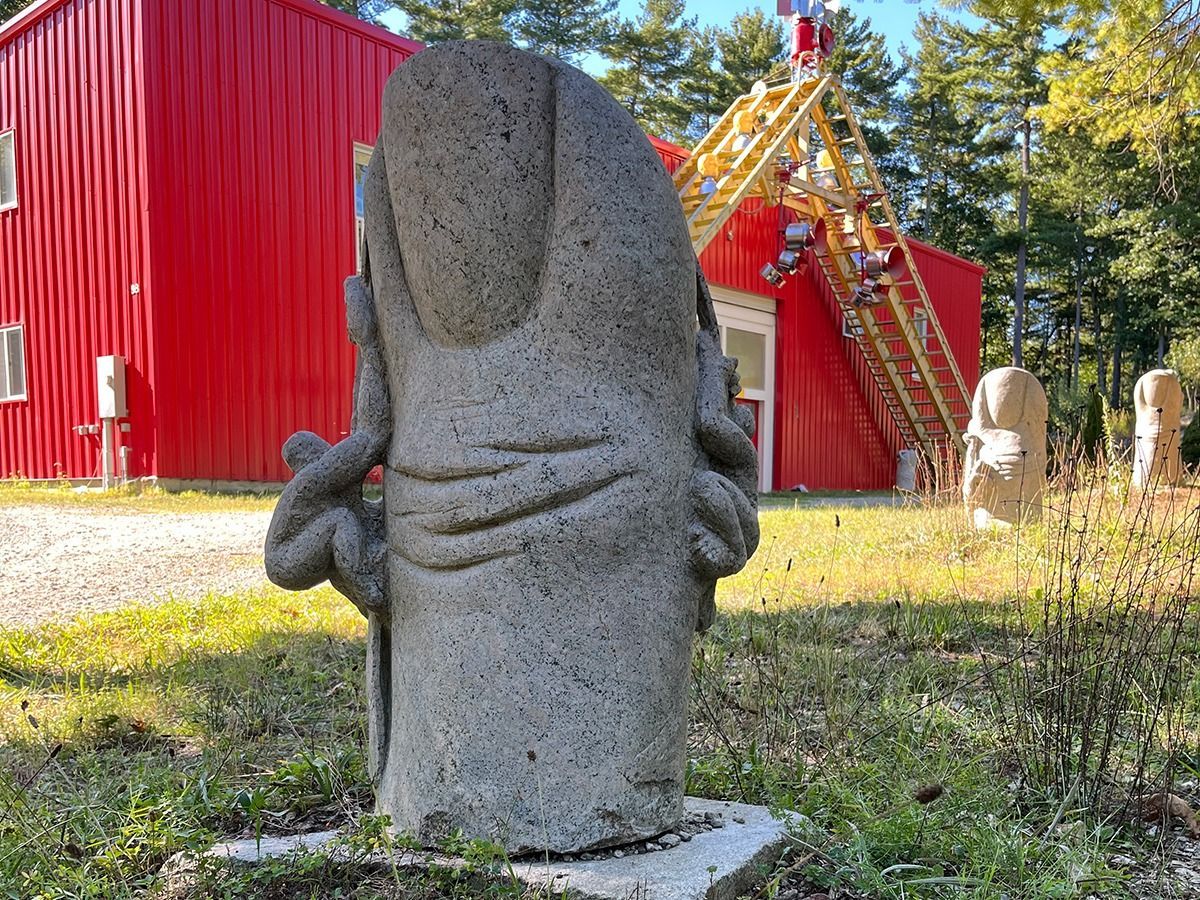 Granite sculpture of a thumb in a grassy yard with a red building in the background.