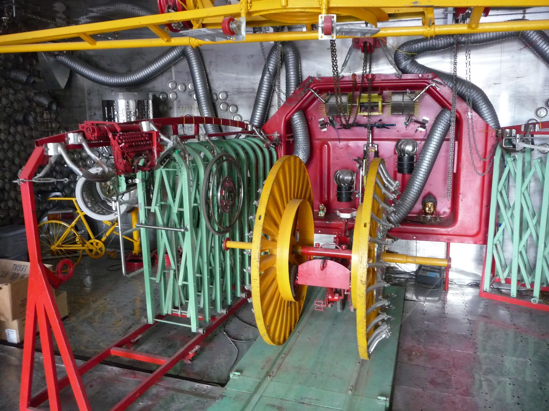 Equipment with a large spool and various mechanical arms, likely for industrial manufacturing, inside a metallic-walled room.