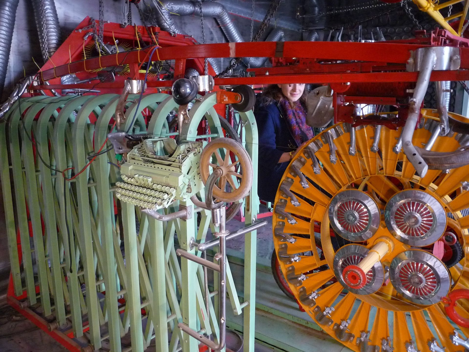 A person stands near a complex, colorful machine made of green, orange, and red components, possibly for an art exhibit.
